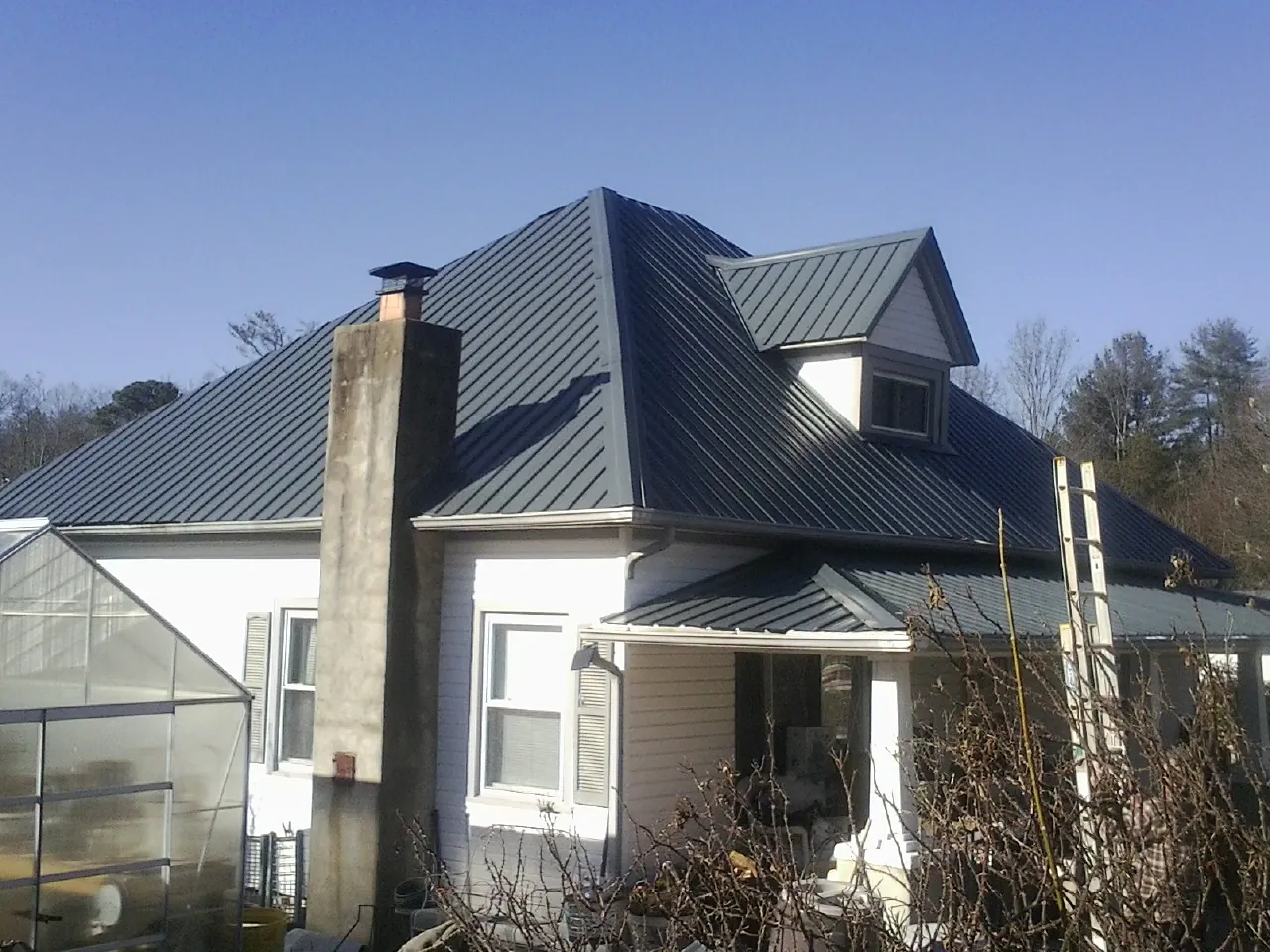 Dark blue standing seam metal roof on a white farmhouse with dormer — Slate & Tile Roof Repair by Roofing Brothers in Malaga