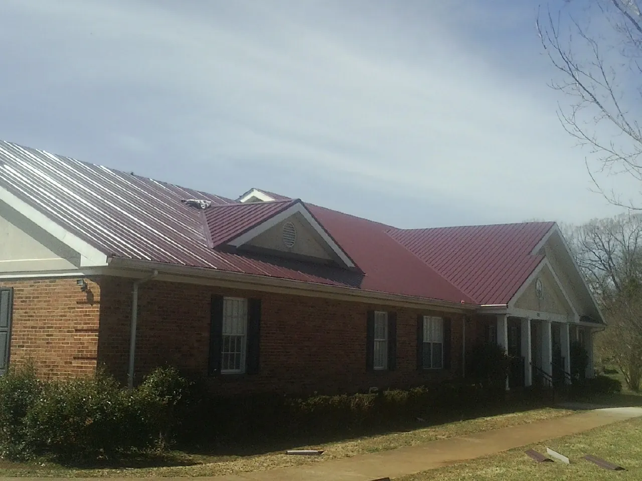 Red metal roof with gabled entries on a long brick building, from a Hail Damage Roof Repair job in Malaga