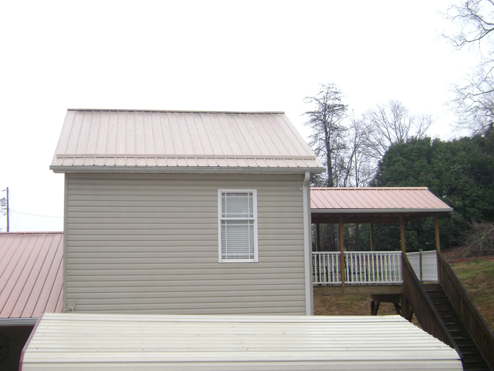 Tan metal roofs on a two story addition and attached porch, from a Roof Replacement job in Malaga